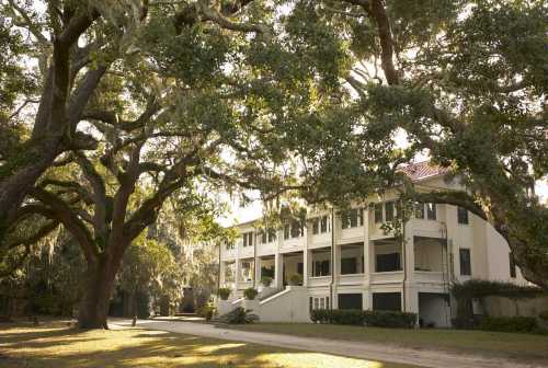 A historic building surrounded by large trees and Spanish moss, set in a serene outdoor landscape.