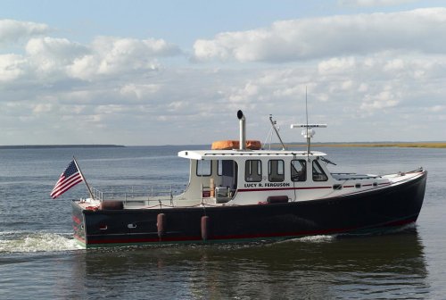 A classic boat named "Lucy R. Ferguson" cruising on calm waters with an American flag displayed.