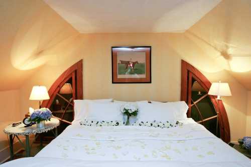 Cozy bedroom with a large bed, decorative pillows, and soft lighting, featuring a floral arrangement and artwork on the wall.