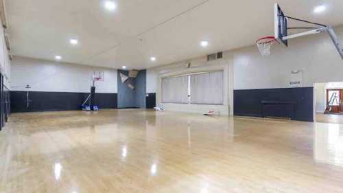 A spacious indoor basketball court with wooden flooring, a hoop, and large windows.