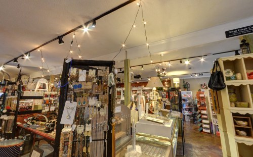 A cozy shop interior filled with jewelry, crafts, and decorative items, illuminated by string lights.