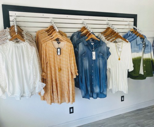 A display of various women's clothing items hanging on a rack, including dresses and tops in different colors and styles.