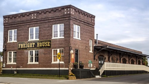 Historic brick building labeled "Freight House" with large windows and a loading dock, set against a cloudy sky.