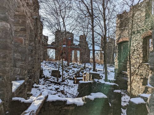 Ruins of a stone building surrounded by trees and snow, with remnants of walls and structures visible.