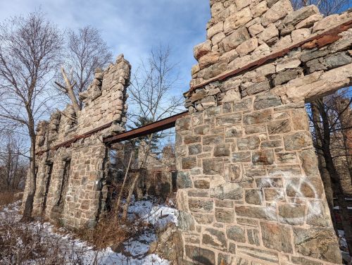 Ruins of a stone structure with exposed beams, surrounded by bare trees and snow under a clear blue sky.
