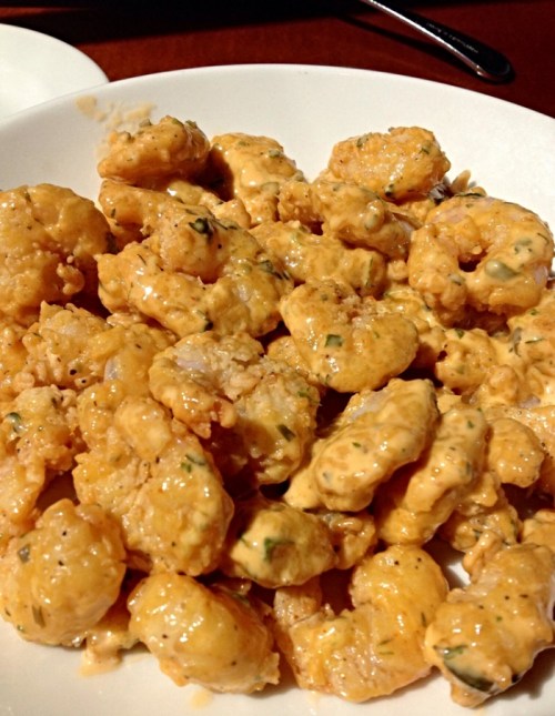 A plate of golden, creamy shrimp coated in a spicy sauce, garnished with herbs.