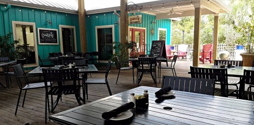 Outdoor dining area with wooden tables and chairs, colorful walls, and a welcoming entrance.