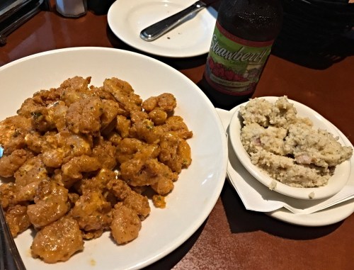 A plate of spicy chicken pieces with a side of mashed potatoes and a bottle of strawberry soda.