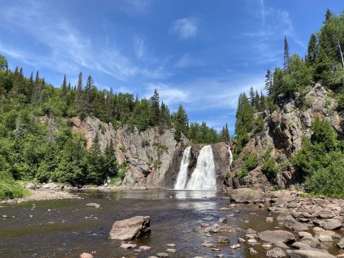 A scenic waterfall surrounded by lush greenery and rocky cliffs under a clear blue sky.
