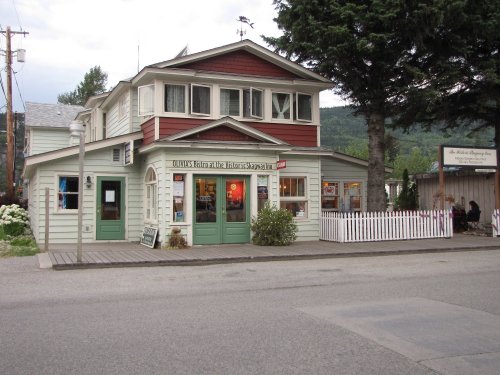 A charming two-story building with red and white siding, featuring a shop front and a white picket fence.