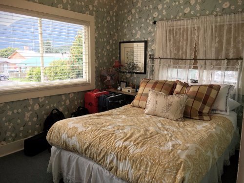 Cozy bedroom with a floral wallpaper, a bed with patterned bedding, and a window overlooking a street.