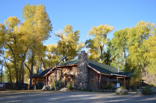 A rustic log cabin surrounded by vibrant autumn trees under a clear blue sky.