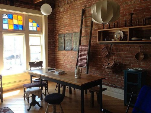 Cozy dining area with a wooden table, brick walls, colorful window, and vintage decor.
