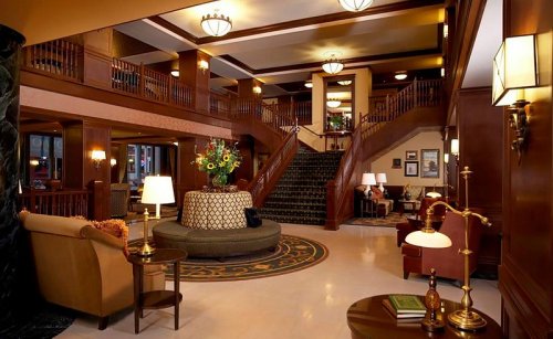Elegant hotel lobby featuring a grand staircase, plush seating, and decorative lighting. Warm wood accents throughout.