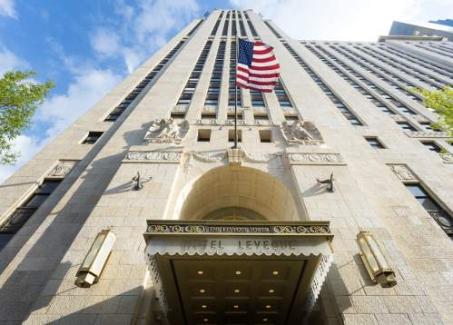View of a tall building with an American flag, featuring ornate entrance and decorative stonework.