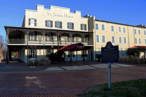 Historic St. James Hotel with a porch, red awning, and nearby historical marker on a sunny day.