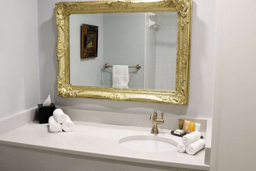 Elegant bathroom with a large ornate mirror, neatly arranged towels, and toiletries on a marble countertop.