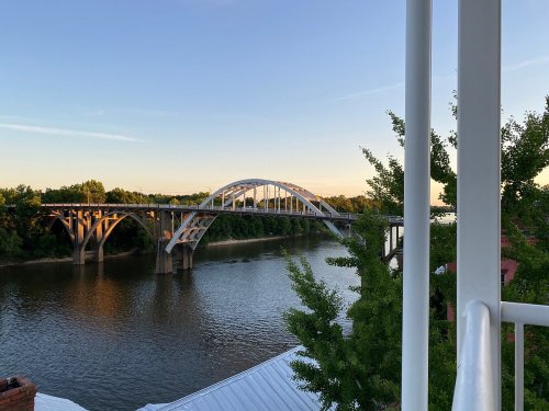 A bridge spans a calm river, framed by trees and a clear sky during sunset.