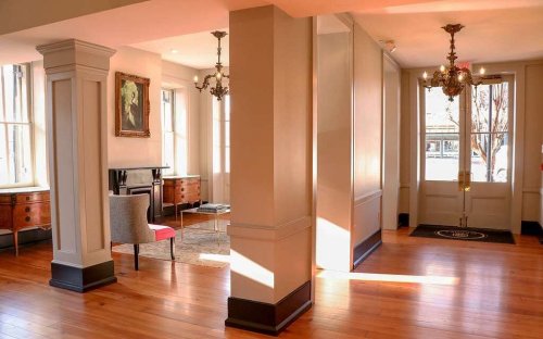 Bright interior of a room with wooden floors, elegant furniture, and large windows, featuring a painting on the wall.