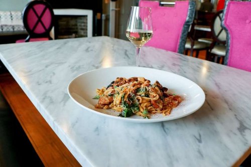 A plate of pasta with sauce and herbs on a marble table, accompanied by a glass of white wine.