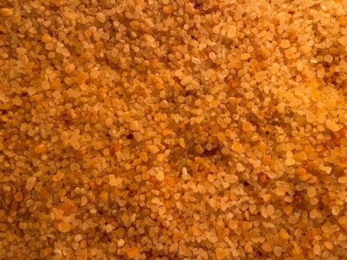 Close-up of a textured surface covered in small, golden-orange granules resembling coarse sand or sugar.