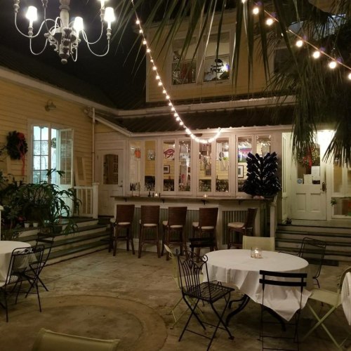 Cozy outdoor dining area with string lights, a bar, and tropical plants, set in a charming, well-lit courtyard.