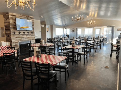 A spacious restaurant interior with checkered tablecloths, chandeliers, and a cozy fireplace.