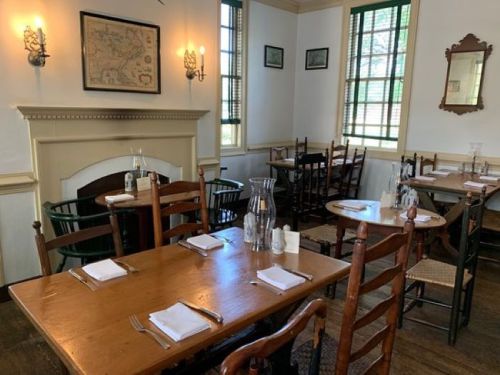 Cozy dining room with wooden tables, chairs, and a fireplace, featuring vintage decor and large windows.