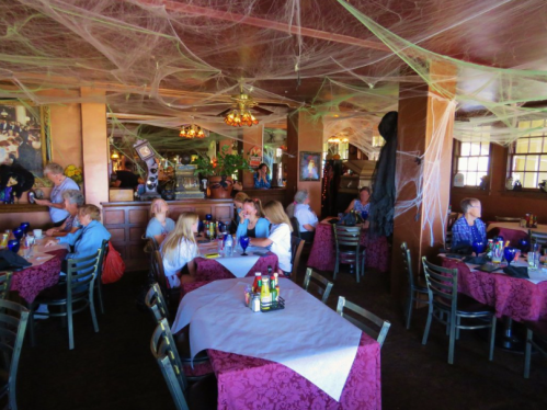 A restaurant decorated for Halloween, featuring cobwebs and a lively atmosphere with diners at tables.