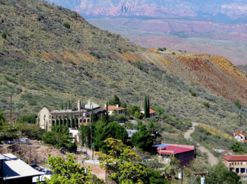 A scenic view of a hillside with buildings, greenery, and mountains in the background under a clear blue sky.