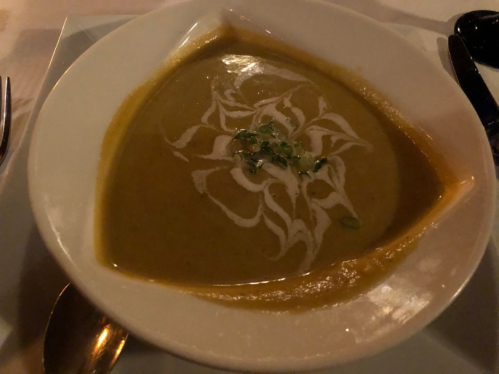 A bowl of creamy soup with a decorative swirl of cream and herbs on top, served in a white dish.