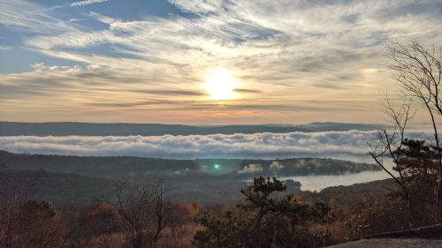 A serene landscape at sunrise, with clouds rolling over hills and a golden sun illuminating the sky.