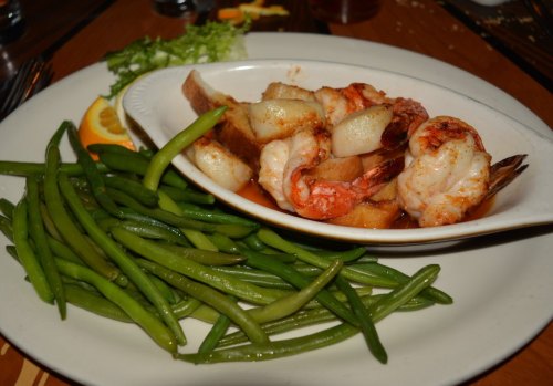 A plate featuring shrimp and scallops in sauce, accompanied by green beans and a side of lettuce and lemon.