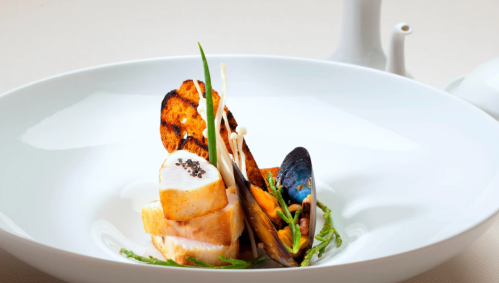 A gourmet dish featuring grilled chicken, mussels, and garnishes on a white plate.