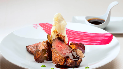A gourmet dish featuring sliced meat, garnished with colorful sauces and herbs, served elegantly on a white plate.