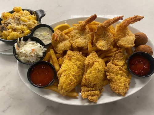 A plate of fried fish, shrimp, fries, coleslaw, and macaroni and cheese, served with dipping sauces.