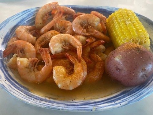 A plate of seasoned shrimp with corn on the cob and a red potato, served in a flavorful broth.