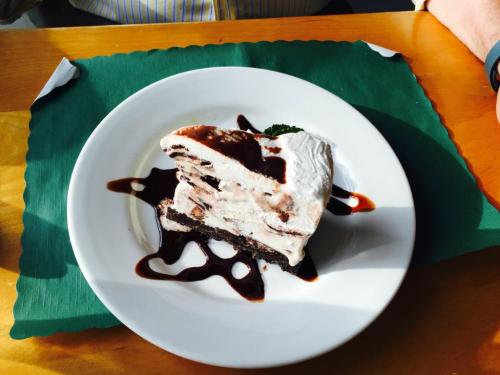 A slice of layered dessert with chocolate, whipped cream, and a drizzle of chocolate sauce on a white plate.