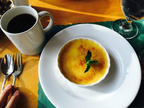 A creamy dessert in a white dish, topped with a mint leaf, beside a cup of coffee and a glass of water.