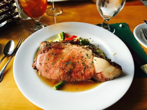 A plate of juicy prime rib with herbs, served with mixed vegetables and a rich sauce, alongside drinks.