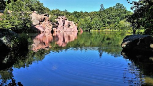 A serene lake surrounded by lush greenery and rocky cliffs, with calm water reflecting the landscape.