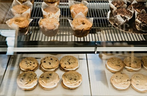 A display case with muffins and cookie sandwiches, showcasing a variety of baked goods.