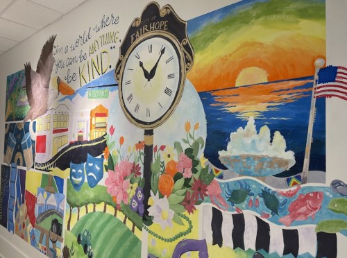 Colorful mural featuring a clock, sunset, flowers, and various symbols of kindness and community in Fairhope.
