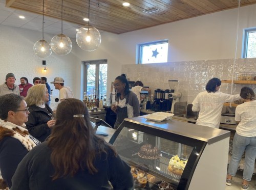 A busy café scene with customers chatting and baristas preparing drinks behind the counter. Warm, inviting atmosphere.
