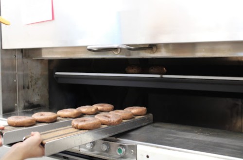 A person holds a tray of freshly baked donuts, ready to be placed in an oven.