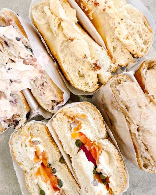 A variety of sandwiches with different fillings, displayed on a light surface, wrapped in paper.