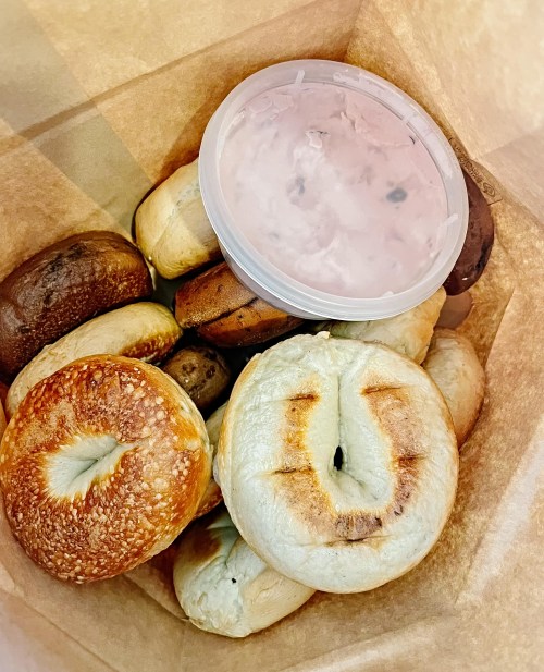 A paper bag filled with assorted bagels and a container of cream cheese.