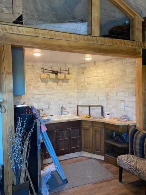 Cozy kitchen area with wooden cabinets, stone walls, and a lofted sleeping space above.