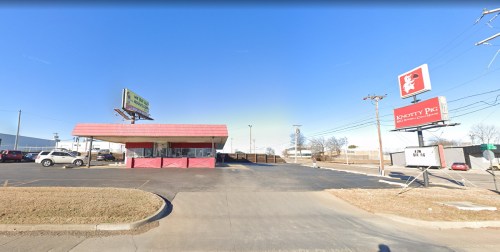 A fast-food restaurant with a red roof and signage, set against a clear blue sky and a parking lot.