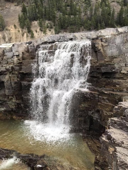 A cascading waterfall flows over rocky cliffs into a serene pool below, surrounded by lush greenery.